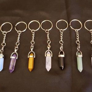 May include: Eight crystal point keychains with silver key rings and chains. The crystals are in various colors, including blue, purple, yellow, pink, white, black, and green.