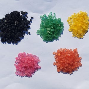 May include: Five piles of colorful sugar crystals. The piles are black, green, yellow, orange, and pink.
