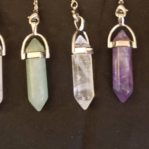 May include: Seven crystal point pendulums with silver chains and metal tops. The crystals are black, white, green, clear, purple, blue, and brown.