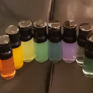 May include: A set of ten small glass bottles with black caps. The bottles are filled with different colored liquids, including orange, yellow, green, blue, purple, and clear.