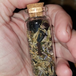 May include: A small glass bottle with a cork stopper filled with dried herbs and flowers. The bottle is clear and the herbs and flowers are a mix of green, brown, and purple.