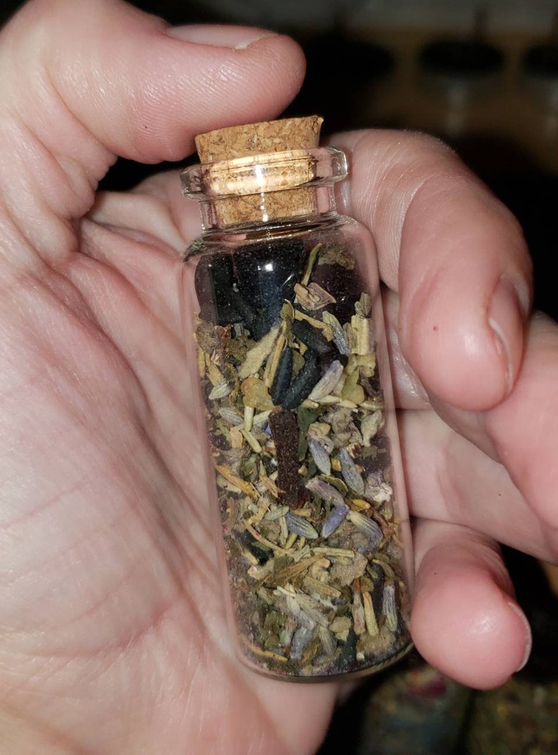 May include: A small glass bottle with a cork stopper filled with dried herbs and flowers. The bottle is clear and the herbs and flowers are a mix of green, brown, and purple.