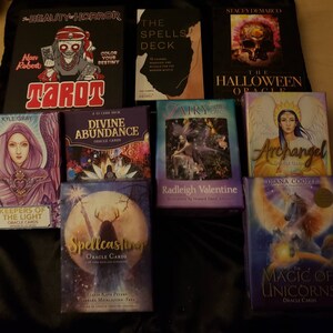 May include: A collection of oracle and tarot card decks, including "Beauty & Horror Tarot", "The Spells Deck", "Divine Abundance Oracle Cards", "Keepers of the Light Oracle Cards", "Spellcasting Oracle Cards", "Airy Fairy Tarot Cards", "Archangel Oracle Cards", "The Magic of Unicorns Oracle Cards", and "The Halloween Oracle".