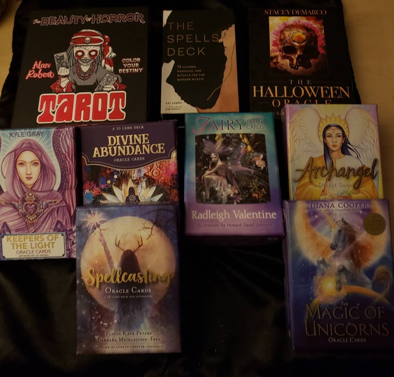 May include: A collection of oracle and tarot card decks, including "Beauty & Horror Tarot", "The Spells Deck", "Divine Abundance Oracle Cards", "Keepers of the Light Oracle Cards", "Spellcasting Oracle Cards", "Airy Fairy Tarot Cards", "Archangel Oracle Cards", "The Magic of Unicorns Oracle Cards", and "The Halloween Oracle".