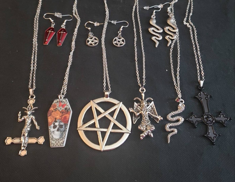 May include: A set of seven silver necklaces with various pendants, including a pentagram, a coffin, a skull, a snake, a demon, and a cross. The necklaces are on a black background.