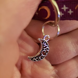 Puede incluir: Encanto de luna creciente de plata con un dise&ntilde;o de filigrana decorativo. El encanto est&aacute; unido a un anillo de plata.