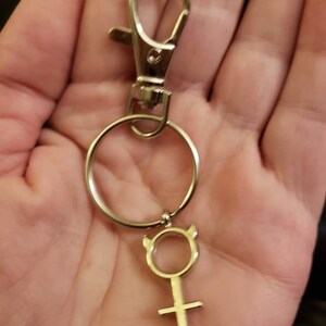 May include: Silver keychain with a silver ring and a silver charm in the shape of a female symbol with horns.