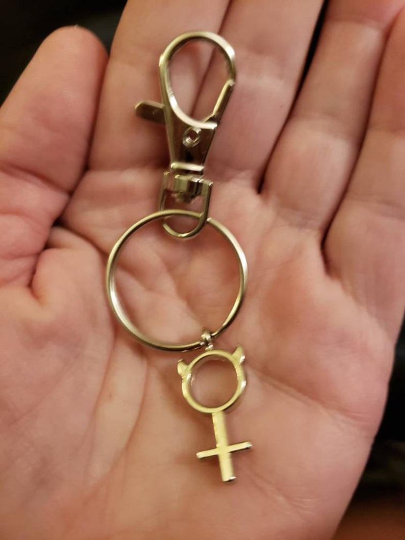 May include: Silver keychain with a silver ring and a silver charm in the shape of a female symbol with horns.