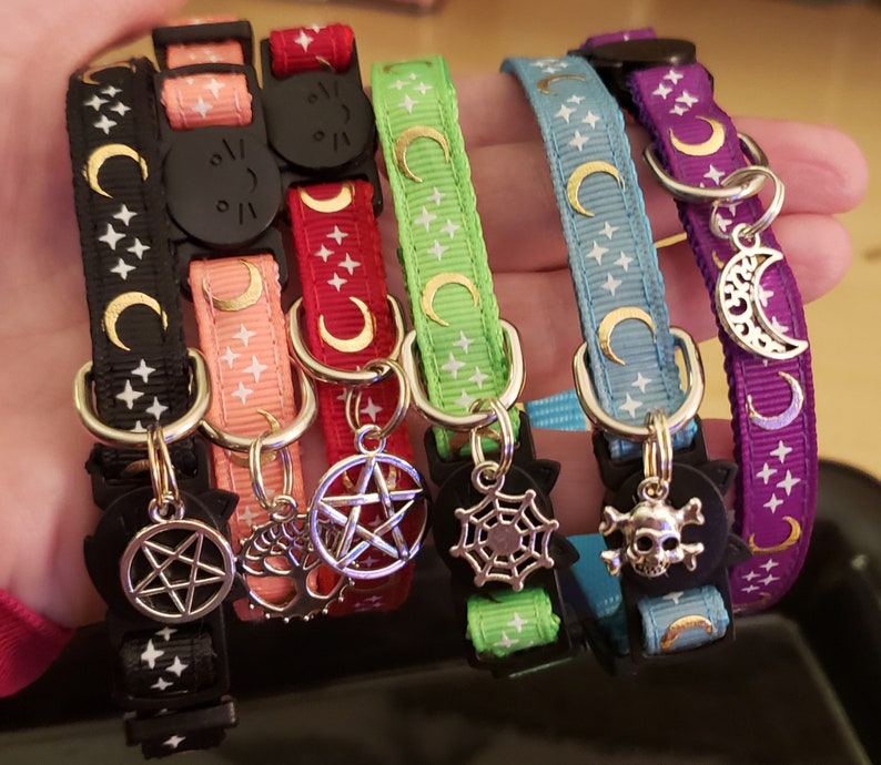 Puede incluir: Cinco collares de gato coloridos con dijes. Los collares est&aacute;n hechos de cinta con un patr&oacute;n de estrellas y tienen dijes de diferentes colores, incluyendo una luna creciente, una telara&ntilde;a, un pentagrama, una calavera y una estrella.