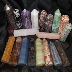 May include: A collection of various crystal towers in shades of purple, pink, green, brown, and white. The crystals have different patterns and textures, with some appearing translucent. The crystals are arranged on a black surface.