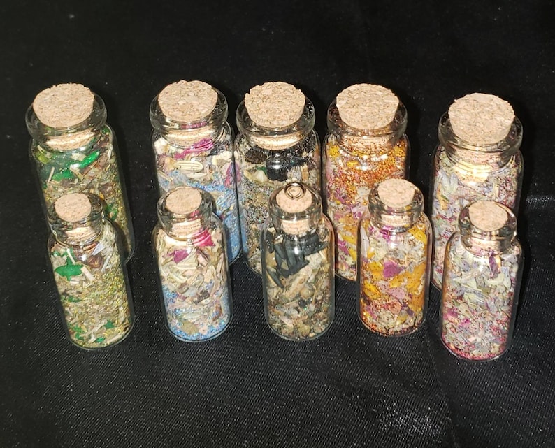May include: Ten small glass bottles with cork tops filled with various dried herbs, flowers, and other natural materials. The bottles are arranged in two rows on a black surface.