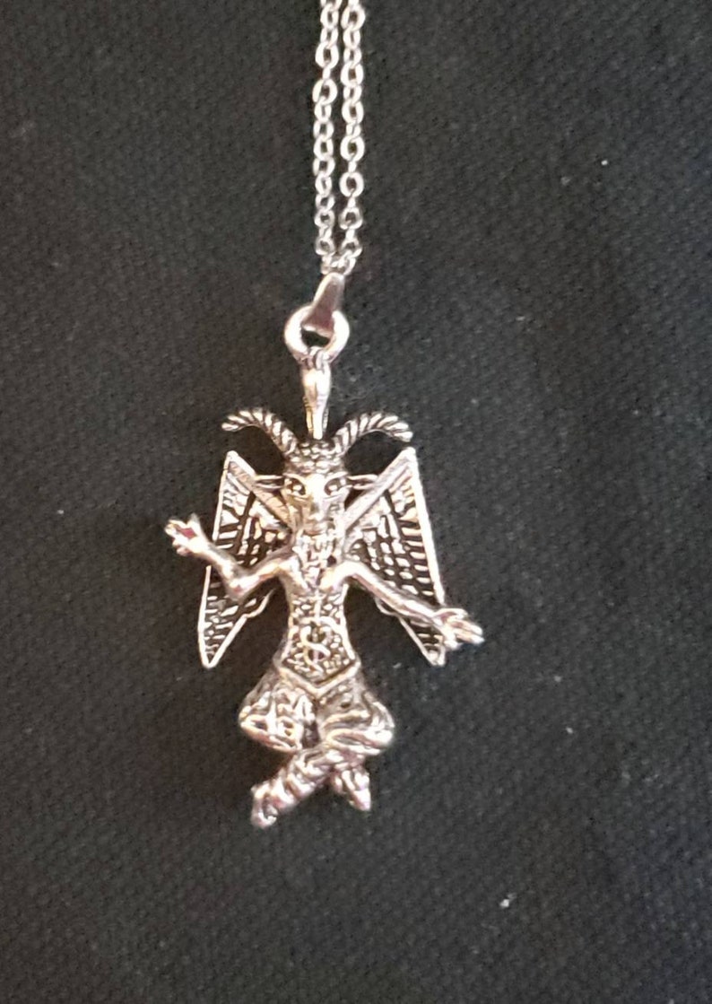 May include: Silver pendant necklace featuring a detailed depiction of a winged demon with horns and a goatee. The pendant is hanging from a silver chain.