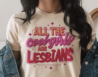 May include: A cream colored t-shirt with the text "All the cool girls are lesbians" in pink and red lettering.