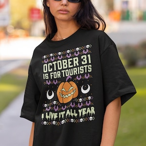 May include: Black t-shirt with a Halloween-themed design. The shirt features the text "OCTOBER 31 IS FOR TOURISTS" above a jack-o'-lantern and the phrase "I LIVE IT ALL YEAR". The design includes bats, skulls, and crescent moons.
