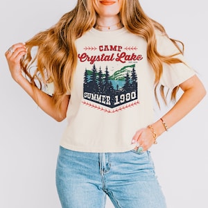 May include: A cream colored t-shirt with a vintage graphic design that says "Camp Crystal Lake Est. 1935 Summer 1980". The graphic features a forest scene with a lake and a baseball diamond.
