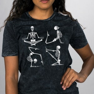 May include: A black t-shirt with a distressed look featuring a graphic of four skeletons in different yoga poses.