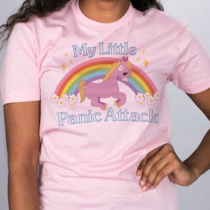 May include: Pink t-shirt with a rainbow and a cartoon unicorn with the text "My Little Panic Attack" printed on it.
