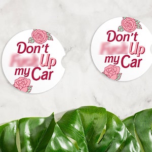 May include: Two white round coasters with pink roses and the text "Don't mess up my Car" in burgundy lettering.