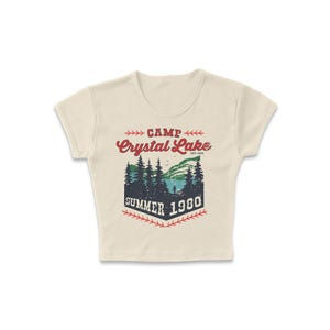 May include: Cream-colored crop top with a graphic design featuring the words "Camp Crystal Lake Summer 1980." The design includes a lake scene with trees and a mountain range, in red, green, and blue.