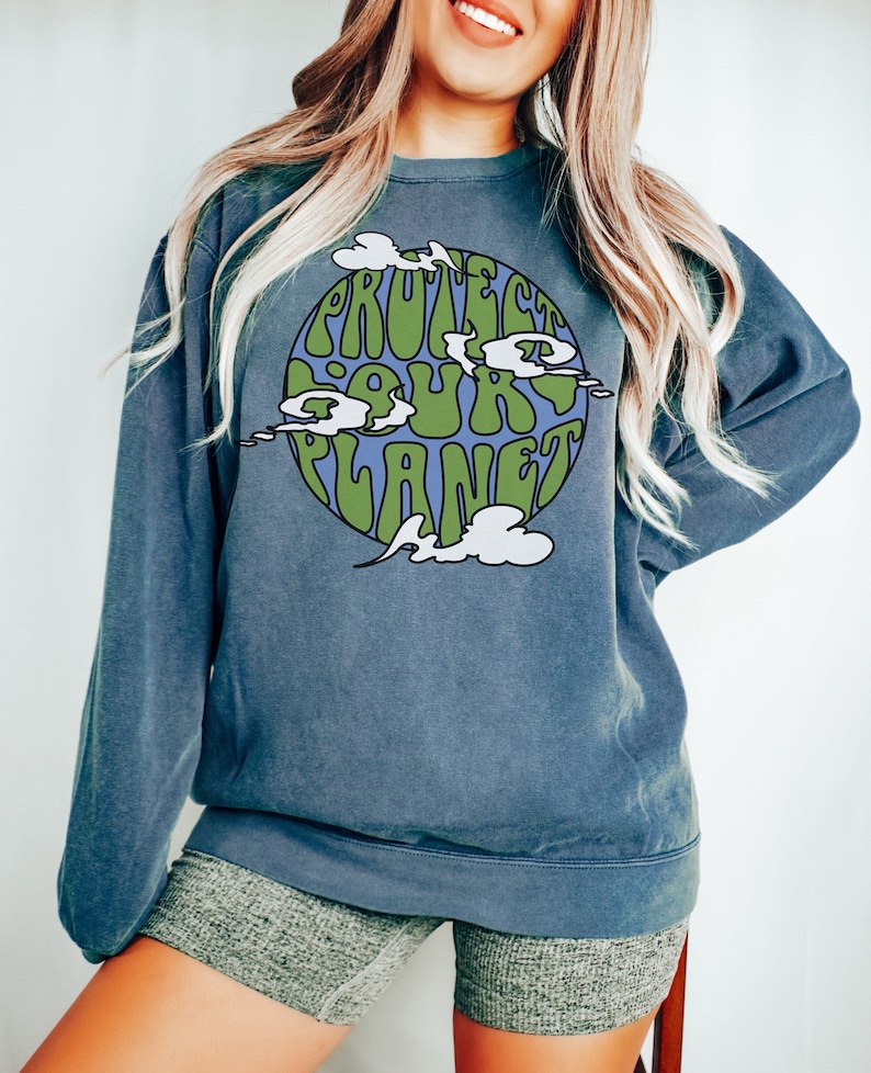 May include: A blue sweatshirt with a green and blue graphic of the Earth with the text "Protect Our Planet" in a retro font.