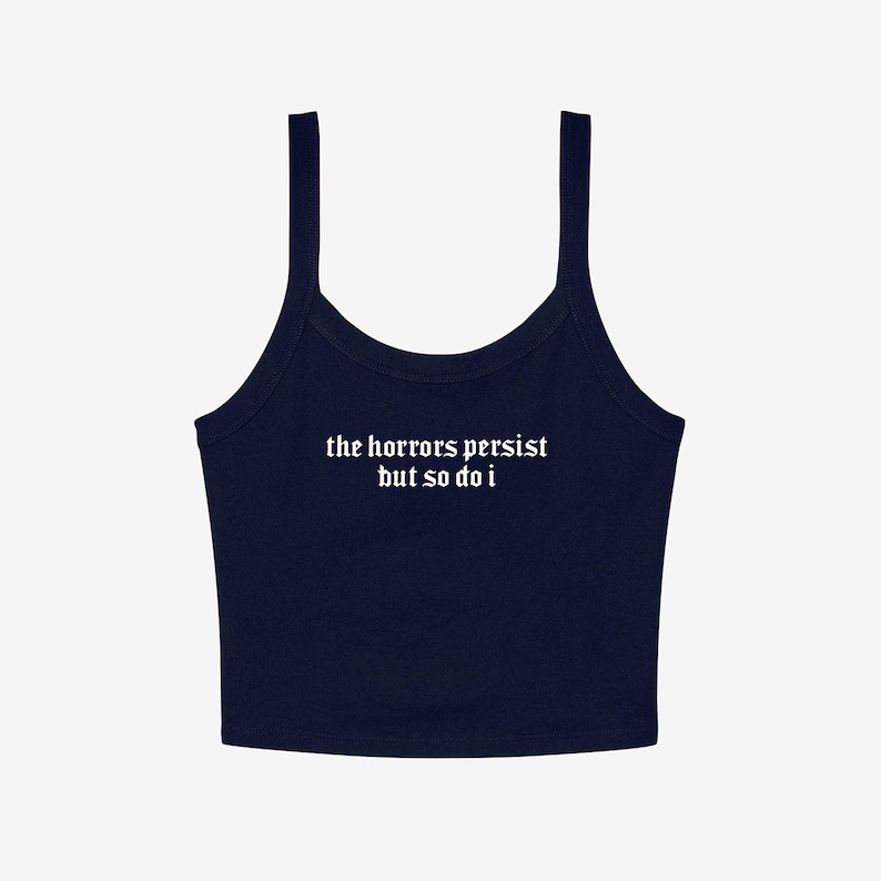 May include: Navy blue crop top with thin straps. The white text on the front reads "the horrors persist but so do i". The top has a scoop neckline and is made of a soft material.