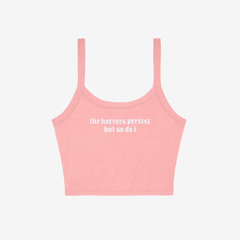 May include: A light pink crop top with thin straps. The text "the horrors persist but so do i" is printed in white across the front. The top is made of a soft, likely cotton, material.
