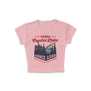 May include: A light pink crop top with a graphic design. The design features the words "Camp Crystal Lake Summer 1980" in red and navy blue, with a scenic illustration of a lake and trees.