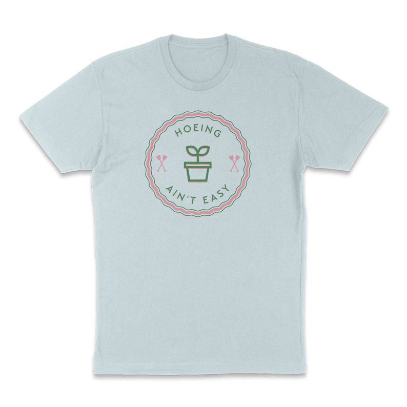 May include: Light blue t-shirt with a green and pink graphic of a plant in a pot with the text "HOEING AIN'T EASY" in a circle.