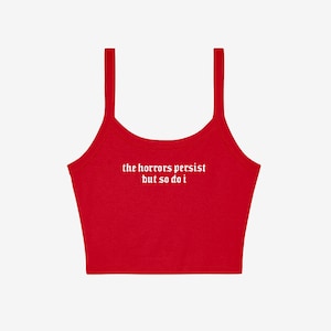 May include: A red crop top with thin straps. The white text "the horrors persist but so do i" is printed across the front. The top is made of a soft material and is suitable for casual wear.