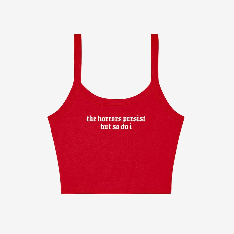 May include: A red crop top with thin straps. The white text "the horrors persist but so do i" is printed across the front. The top is made of a soft material and is suitable for casual wear.