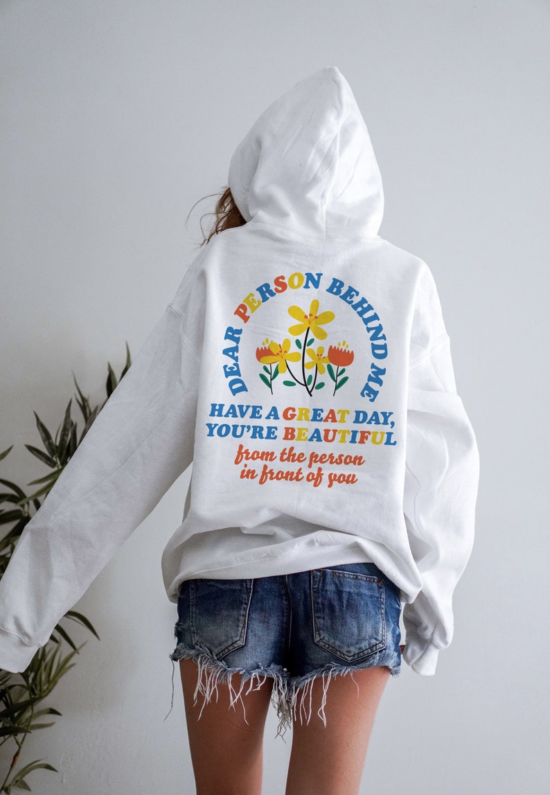 May include: White hoodie with a colorful graphic on the back that says "Dear Person Behind Me Have a Great Day, You're Beautiful from the person in front of you".