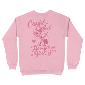 May include: Pink sweatshirt with a graphic of a cupid with a heart and the text "Cupid Called He wants me to Block You".