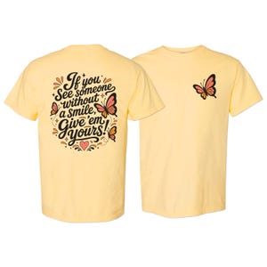 May include: A pale yellow t-shirt featuring a small butterfly graphic on the front left chest and a large back print with the text If you see someone without a smile, give 'em yours! surrounded by decorative butterflies, stars, and a heart.