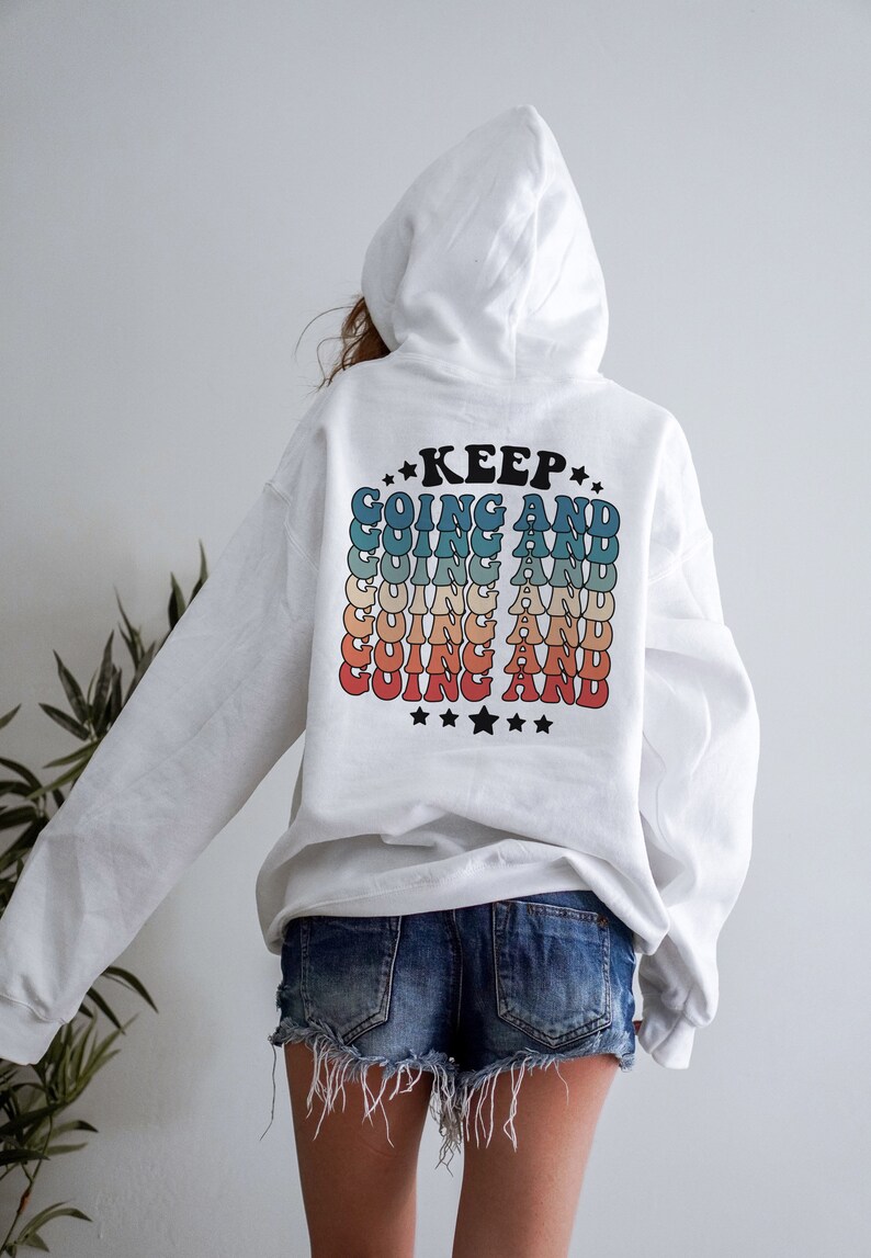 Puede incluir: Sudadera con capucha blanca con un gr&aacute;fico de estilo retro en la espalda que dice "KEEP GOING AND" repetido en un arco&iacute;ris de colores.