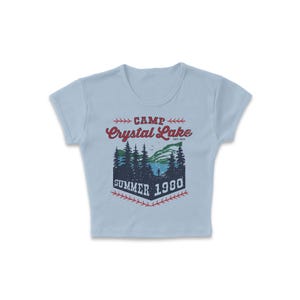 May include: Light blue crop top with a graphic featuring the text "CAMP Crystal Lake SUMMER 1980". The graphic depicts a lake scene with trees and a person. The text is in red and navy blue.
