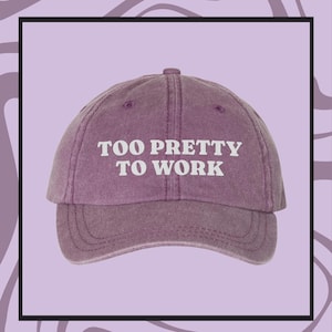 May include: A purple baseball cap with the text "TOO PRETTY TO WORK" in white.