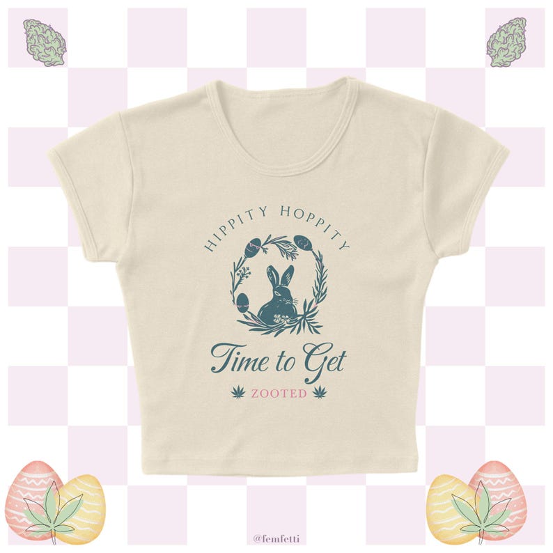 May include: A cream-colored cropped t-shirt with a blue graphic of a bunny rabbit in a wreath with the text "Hippity Hoppity Time to Get Zooted".
