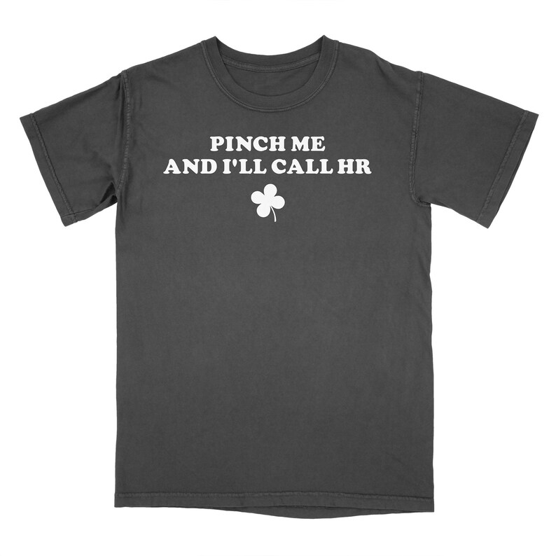 Peut inclure: Un t-shirt gris fonc&eacute; avec le texte "Pinch me and I'll call HR" en lettres blanches. Un tr&egrave;fle &agrave; quatre feuilles blanc se trouve sous le texte.