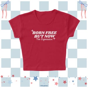 May include: A red crop top with the text "BORN FREE BUT NOW I'm Expensive" in white. The top has short sleeves and a scoop neck. The background features a blue and white checkered pattern with star and ribbon accents.