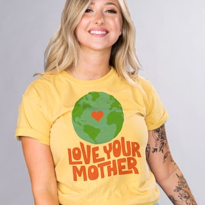 May include: A yellow t-shirt with a green and blue globe graphic and the text "LOVE YOUR MOTHER" in orange and red. The globe has a red heart in the center.