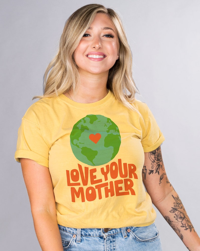 May include: A yellow t-shirt with a green and blue globe graphic and the text "LOVE YOUR MOTHER" in orange and red. The globe has a red heart in the center.