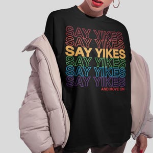 May include: Black t-shirt with a rainbow design that says "Say Yikes" six times and "And Move On" at the bottom.