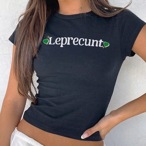 May include: Black cropped t-shirt with a white graphic that says "Leprecumt" with two green hearts on either side of the text.