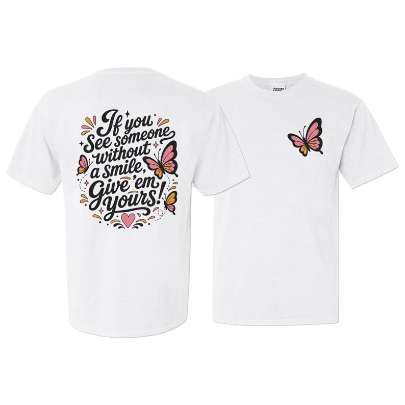 May include: A white short-sleeve t-shirt featuring a small pink and orange butterfly on the front chest. The back displays the text "If you see someone without a smile, Give 'em yours!" surrounded by butterflies, a pink heart, and small stars.