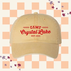 May include: A tan baseball cap with a red embroidered logo that says "Camp Crystal Lake Est. 1935".