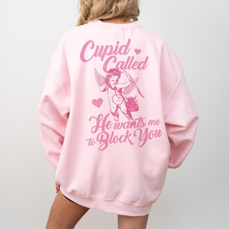 May include: Pink sweatshirt with a graphic of Cupid on the phone with the text "Cupid Called He wants me to Block You" in pink.