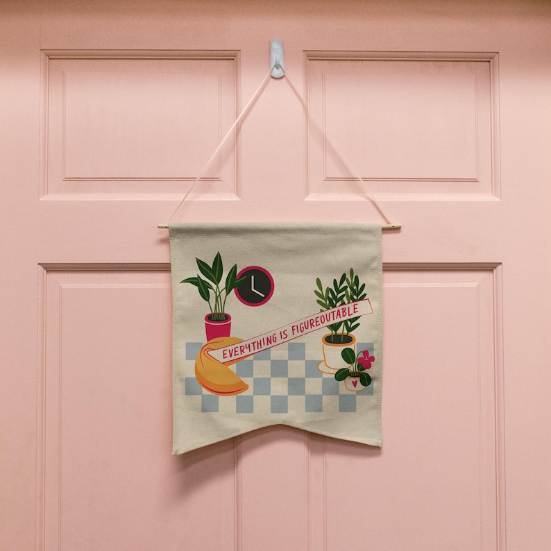 May include: A white canvas banner with the text "Everything is Figureoutable" hanging on a pink door. The banner features a fortune cookie, two potted plants, and a clock.