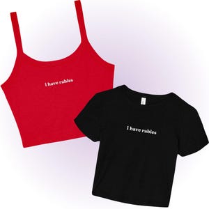 May include: A red crop top with spaghetti straps and a black t-shirt, both with the white text "i have rabies". The crop top is a solid red color, and the t-shirt is black.
