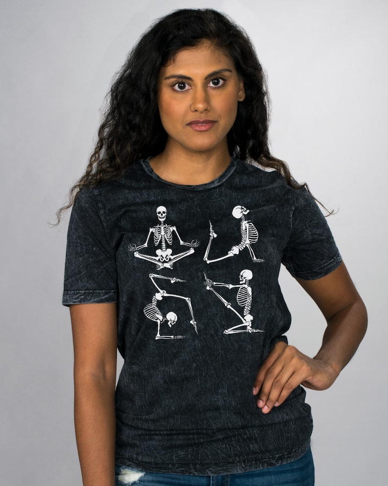 May include: A black t-shirt with a distressed look featuring a graphic of four skeletons in different yoga poses.