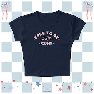May include: Navy blue crop top with the text "FREE TO BE A Little CUNT" in white and red lettering. The top has a scoop neck and short sleeves. The background has a checkered pattern with red and blue stars and bows.